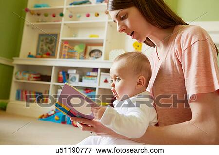 Stock Photo - Mid adult woman and baby daughter reading storybook in playroom. Fotosearch