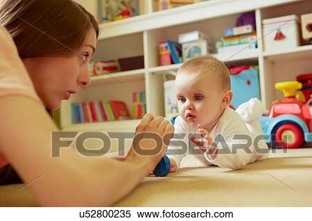 Stock Photography - Mid adult woman and baby daughter playing on playroom floor. Fotosearch
