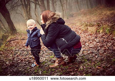 Stock Image - Mid adult woman crouching with toddler son in autumn forest. Fotosearch