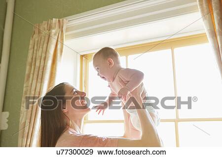 Mid adult woman holding up baby daughter in bedroom View Large Photo Image Stock Photo - Mid adult woman holding up baby daughter in bedroom. Fotosearch