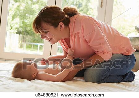 Mid adult woman kneeling on floor playing with baby son View Large Photo Image Stock Image - Mid adult woman kneeling on floor playing with baby son. Fotosearch
