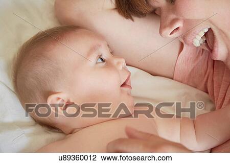 Stock Image - Mid adult woman on bed gazing at baby son. Fotosearch