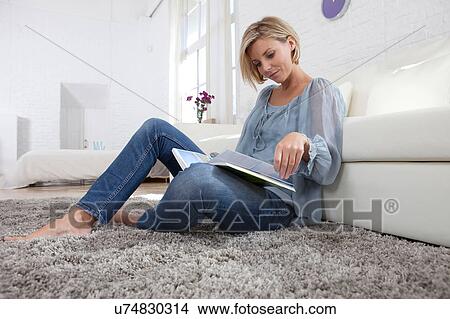 Mid adult woman sitting on rug reading book View Large Photo Image Picture - Mid adult woman sitting on rug reading book. Fotosearch