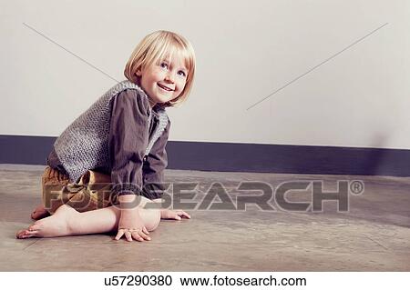 Stock Image - Mischievous girl kneeling on floor. Fotosearch