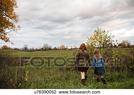 Stock Image - Mother and daughter holding hands walking in meadow, Lakefield, Ontario, Canada. Fotosearch