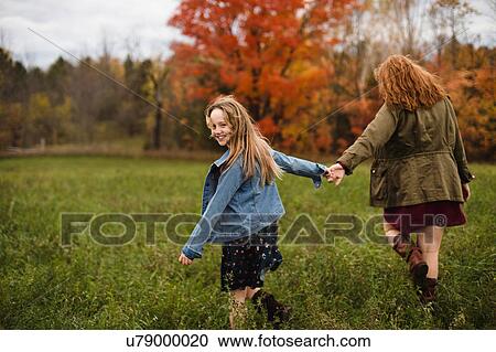 Stock Image - Mother and daughter holding hands walking in meadow, Lakefield, Ontario, Canada. Fotosearch