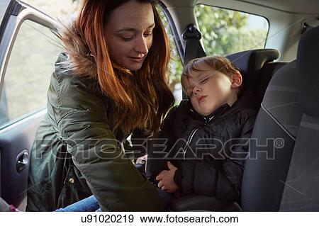 Stock Photo - Mother removing sleeping toddler son from car backseat. Fotosearch