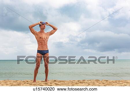 Muscular male swimmer standing on beach putting on swimming goggles View Large Photo Image Stock Image - Muscular male swimmer standing on beach putting on swimming goggles. Fotosearch