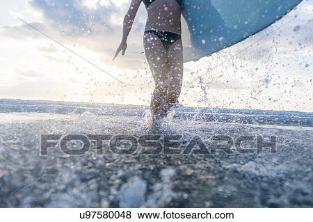 Neck down view of woman carrying surfboard and splashing in sea, Nosara, Guanacaste Province, Costa Rica View Large Photo Image Stock Photo - Neck down view of woman carrying surfboard and splashing in sea, Nosara, Guanacaste Province, Costa Rica. Fotosearch