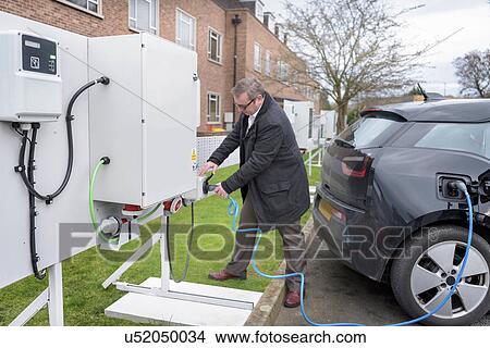 Picture - Office worker charging electric car at charging station. Fotosearch