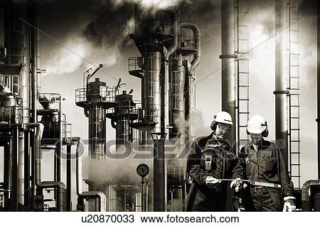 Stock Image - Oil refinery workers and pipework. Fotosearch