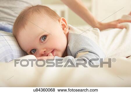 Stock Photo - Portrait of baby girl lying on bed with mother. Fotosearch