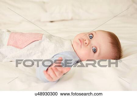 Stock Image - Portrait of blue eyed baby girl lying on bed. Fotosearch