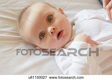 Stock Photo - Portrait of blue eyed baby girl lying on bed. Fotosearch