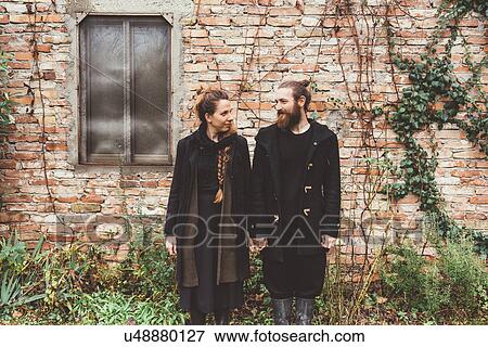 Stock Photo - Portrait of couple holding hands by outbuilding. Fotosearch