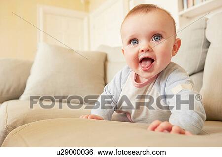 Stock Photograph - Portrait of cute blue eyed baby girl on sofa. Fotosearch