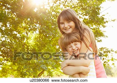 Portrait of girl being hugged by big sister in park View Large Photo Image Stock Photograph - Portrait of girl being hugged by big sister in park. Fotosearch