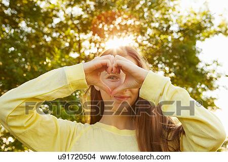 Picture - Portrait of girl making heart shape with hands in park. Fotosearch