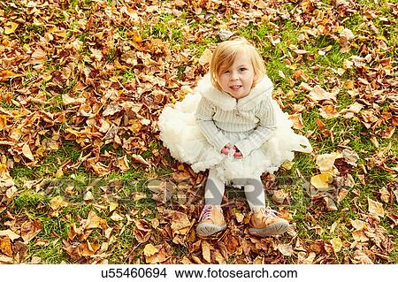 Picture - Portrait of girl sitting in autumn leaves looking at camera smiling. Fotosearch