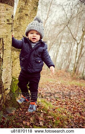 Stock Photo - Portrait of male toddler in knitted hat leaning against forest tree. Fotosearch