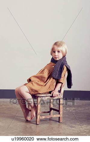 Stock Image - Portrait of sullen girl sitting on old wooden chair. Fotosearch