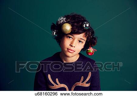 Stock Photograph - Portrait of teenage boy wearing Christmas jumper, and baubles in hair. Fotosearch