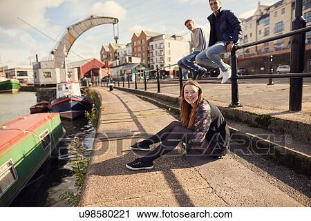 Stock Image - Portrait of three friends sitting beside river, Bristol, UK. Fotosearch