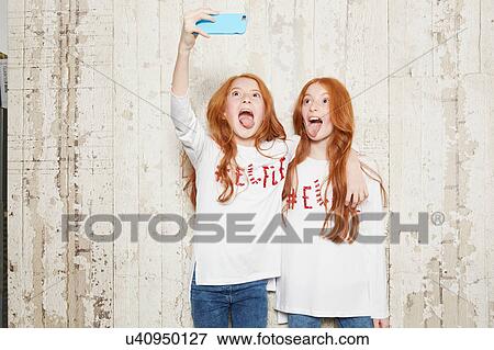 Portrait of twin sisters wearing Christmas jumpers, taking selfie using smartphone View Large Photo Image Stock Photo - Portrait of twin sisters wearing Christmas jumpers, taking selfie using smartphone. Fotosearch