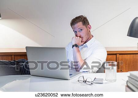 Portrait of worried young businessman at desk using laptop View Large Photo Image Stock Image - Portrait of worried young businessman at desk using laptop. Fotosearch