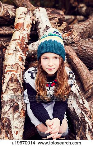 Picture - Portrait of young girl, sitting on log pile. Fotosearch