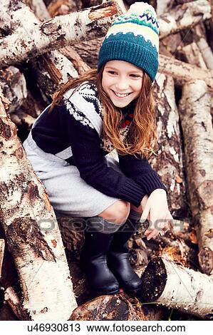 Stock Image - Portrait of young girl, sitting on log pile. Fotosearch