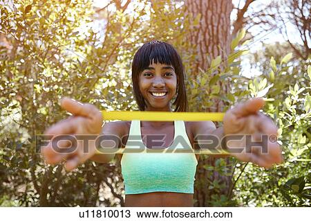 Stock Image - Portrait of young in rural setting, exercising using resistance band. Fotosearch