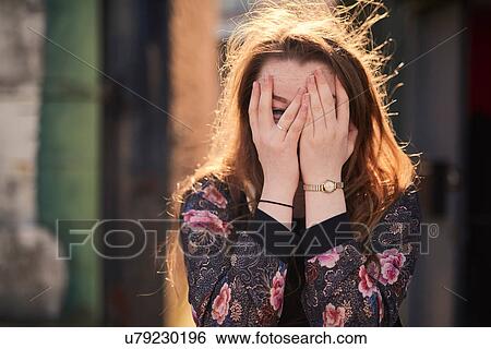 Stock Photograph - Portrait of young woman covering face with hands, Bristol, UK. Fotosearch