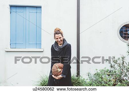 Stock Image - Portrait of young woman holding pumpkin in front of building. Fotosearch