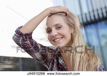 Stock Photo - Portrait of young woman in city with hand in long blond hair. Fotosearch