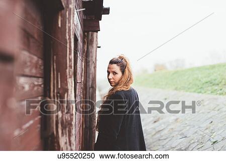 Portrait of young woman looking over her shoulder by weathered hut View Large Photo Image Stock Image - Portrait of young woman looking over her shoulder by weathered hut. Fotosearch