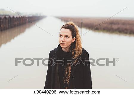 Stock Photograph - Portrait of young woman on misty canal waterfront. Fotosearch