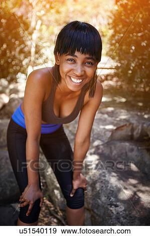 Portrait of young woman outdoors, hands on knees, smiling View Large Photo Image Stock Photo - Portrait of young woman outdoors, hands on knees, smiling. Fotosearch