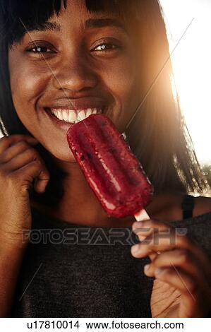 Portrait of young woman, outdoors, eating ice lolly View Large Photo Image Picture - Portrait of young woman, outdoors, eating ice lolly. Fotosearch