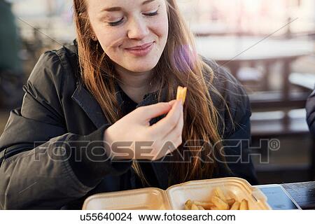 Picture - Portrait of young woman, outdoors, eating chips, Bristol, UK. Fotosearch