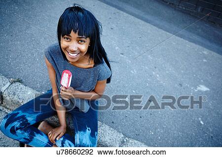 Stock Image - Portrait of young woman, outdoors, eating ice lolly, elevated view. Fotosearch