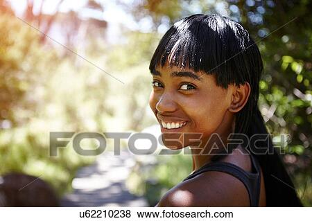 Portrait of young woman, outdoors, looking over shoulder, smiling View Large Photo Image Stock Photo - Portrait of young woman, outdoors, looking over shoulder, smiling. Fotosearch