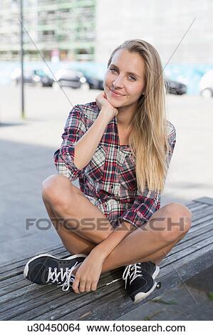 Portrait of young woman sitting cross legged on city bench View Large Photo Image Picture - Portrait of young woman sitting cross legged on city bench. Fotosearch