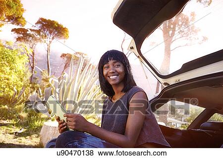 Portrait of young woman sitting in open car boot, holding digital tablet View Large Photo Image Stock Photo - Portrait of young woman sitting in open car boot, holding digital tablet. Fotosearch