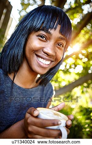 Portrait of young woman sitting outdoors, holding coffee cup, smiling View Large Photo Image Picture - Portrait of young woman sitting outdoors, holding coffee cup, smiling. Fotosearch