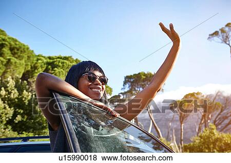 Portrait of young woman standing beside car, leaning on open car door, waving View Large Photo Image Stock Photo - Portrait of young woman standing beside car, leaning on open car door, waving. Fotosearch
