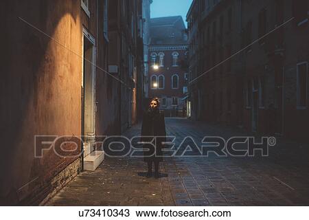 Stock Image - Portrait of young woman standing in street at dusk, Venice, Italy. Fotosearch