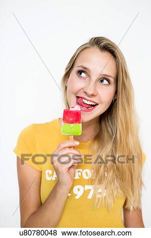 Stock Photo - Portrait of young woman with eating ice lolly against white background. Fotosearch