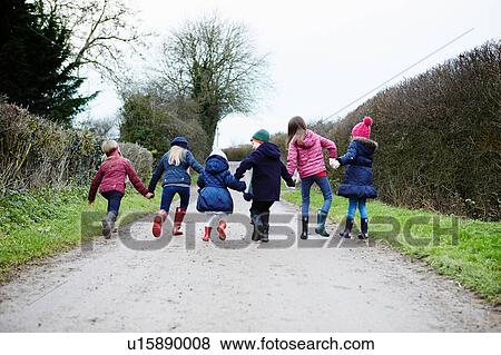 Stock Photo - Rear view of boy and girls holding hands and fooling around on rural road. Fotosearch