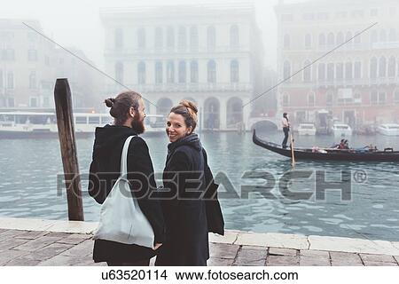 Picture - Rear view of couple on misty canal waterfront, Venice, Italy. Fotosearch